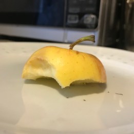 The top section of a red apple sitting on a plate. The apple has been eaten from the bottom up.